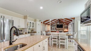 A kitchen with white cabinets, granite countertops, stainless steel appliances, and a dining area with white chairs and a wooden table. - Patio + Pool Table: Lake Marion Getaway (Santee)