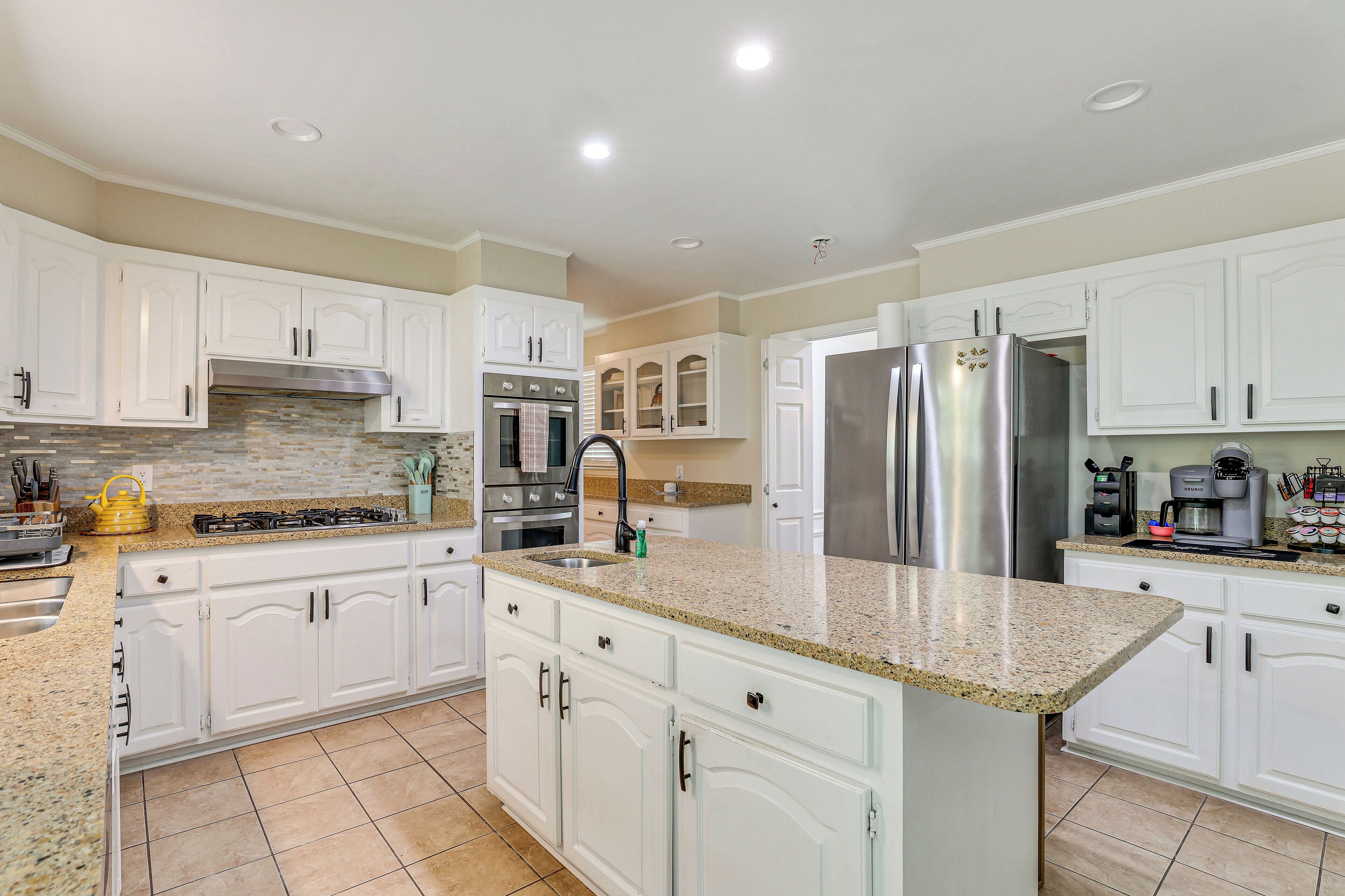 A kitchen with white cabinets, a granite countertop, stainless steel appliances, and a tiled backsplash.