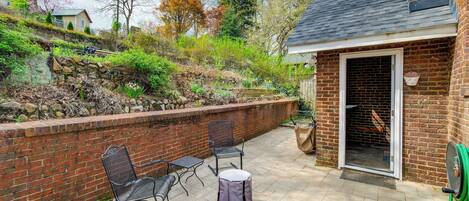 An outdoor patio with a brick wall, two metal chairs, a small round table, and a green garden hose.