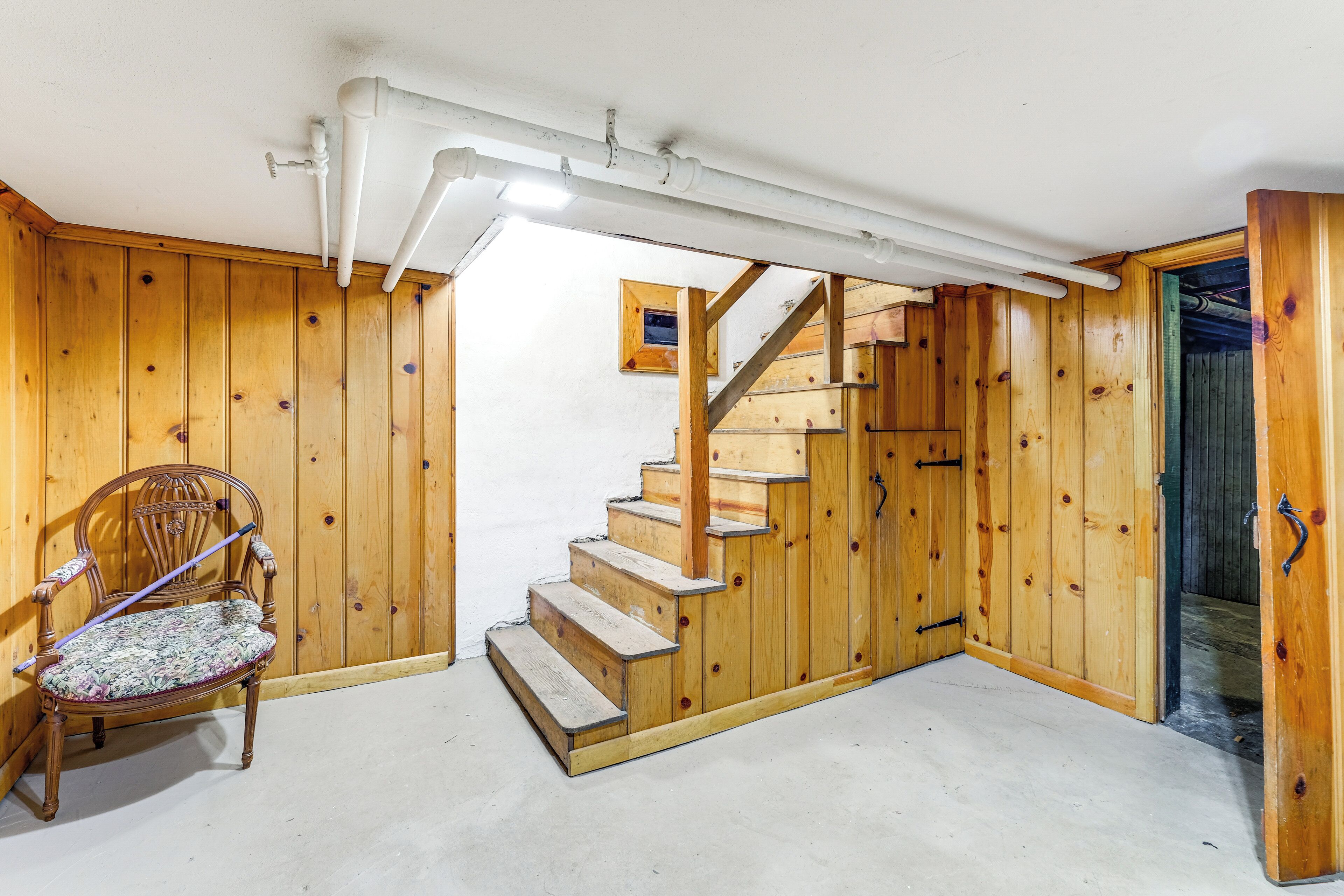 A wooden interior with a chair, a staircase, and a door.