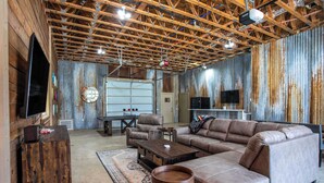 A rustic interior with exposed wooden beams, a large sectional sofa, a coffee table, and a flat-screen TV mounted on the wall. - King Beds, Game Room, On 290, Large Estate,Kitchen (Fredericksburg)