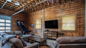 A log cabin interior with a basketball hoop, leather sofas, a TV, and a wooden cabinet. - King Beds, Game Room, On 290, Large Estate,Kitchen (Fredericksburg)