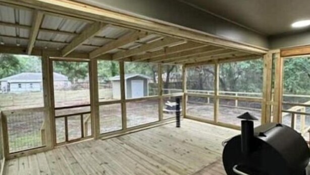 A covered outdoor area with a barbecue grill, wooden flooring, and large windows. - Serenity Cottage (Ocean Springs)