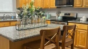 A kitchen with wooden cabinets, a granite countertop, a stainless steel oven, and two bar stools. - Serenity Cottage (Ocean Springs)