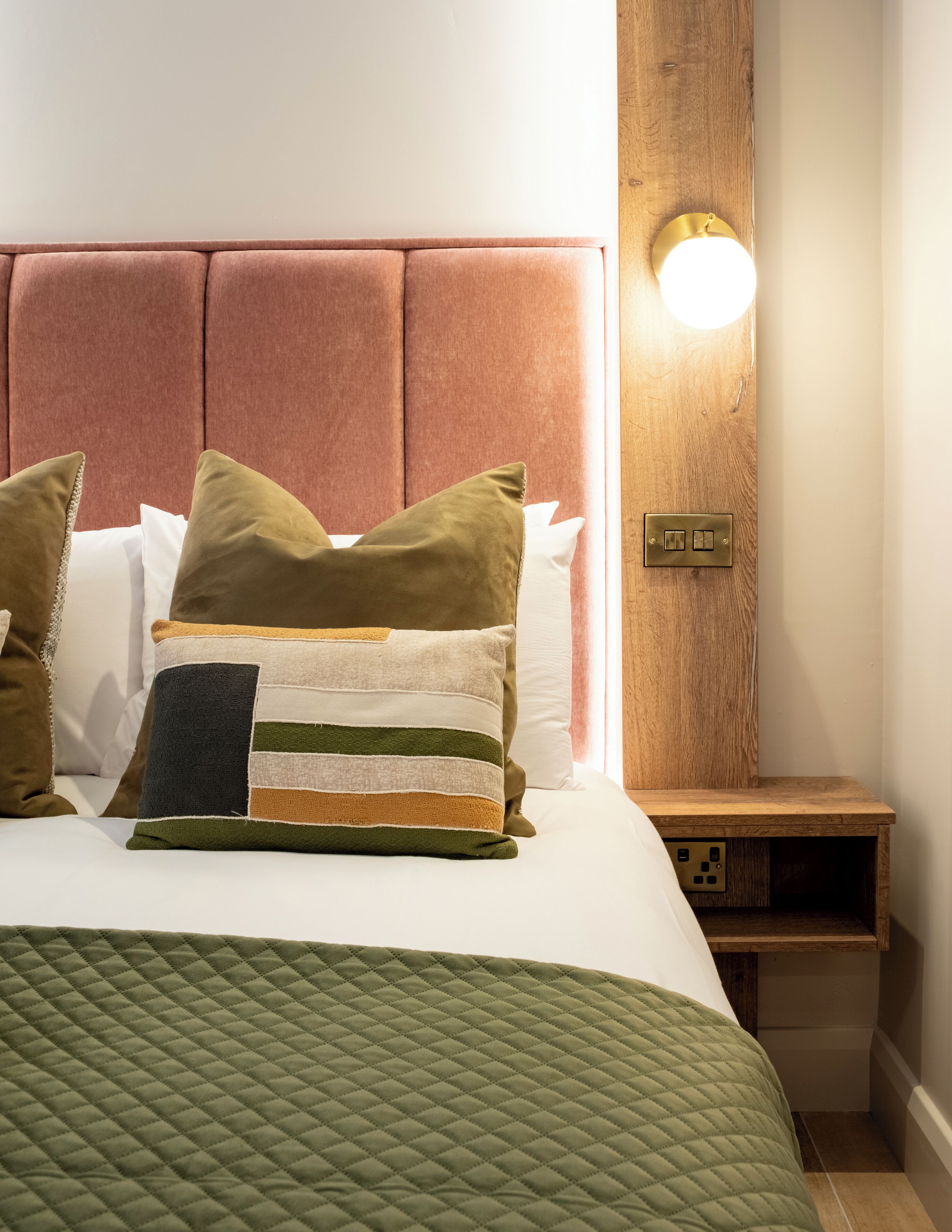 A neatly made bed with a green quilt, a variety of pillows, and a wooden headboard.