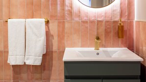 Ein Badezimmer mit rosa gefliesten Wänden, einem weißen Waschbecken und einem Spiegel.