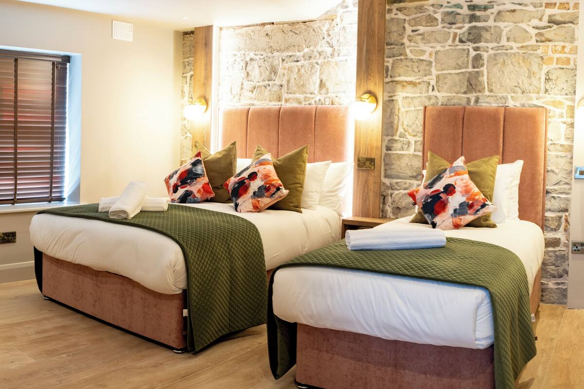 Ein Hotelzimmer mit zwei Betten, jeweils mit Kopfteil, einer Steinsäule und einem Fenster mit Jalousien.