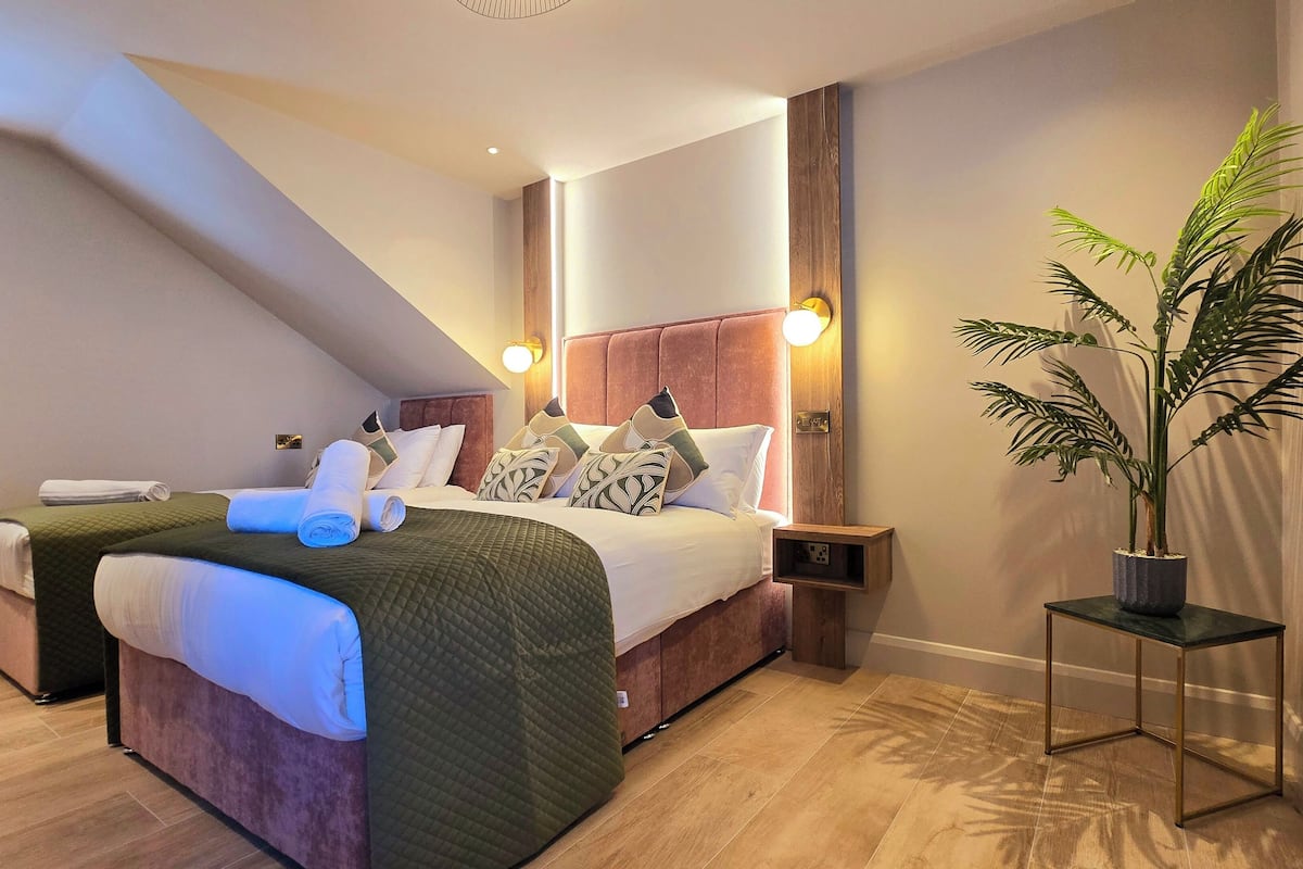 Ein Hotelzimmer mit einem großen Bett, einem Nachttisch, einer Zimmerpflanze und Blick ins Freie.