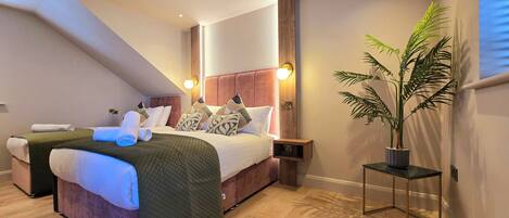 A hotel room with a large bed, a bedside table, a nightstand, a potted plant, and a view of the outside.