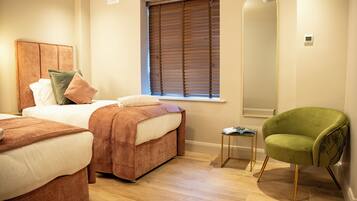 A bedroom with two beds, a green armchair, a bedside table, and a large mirror.