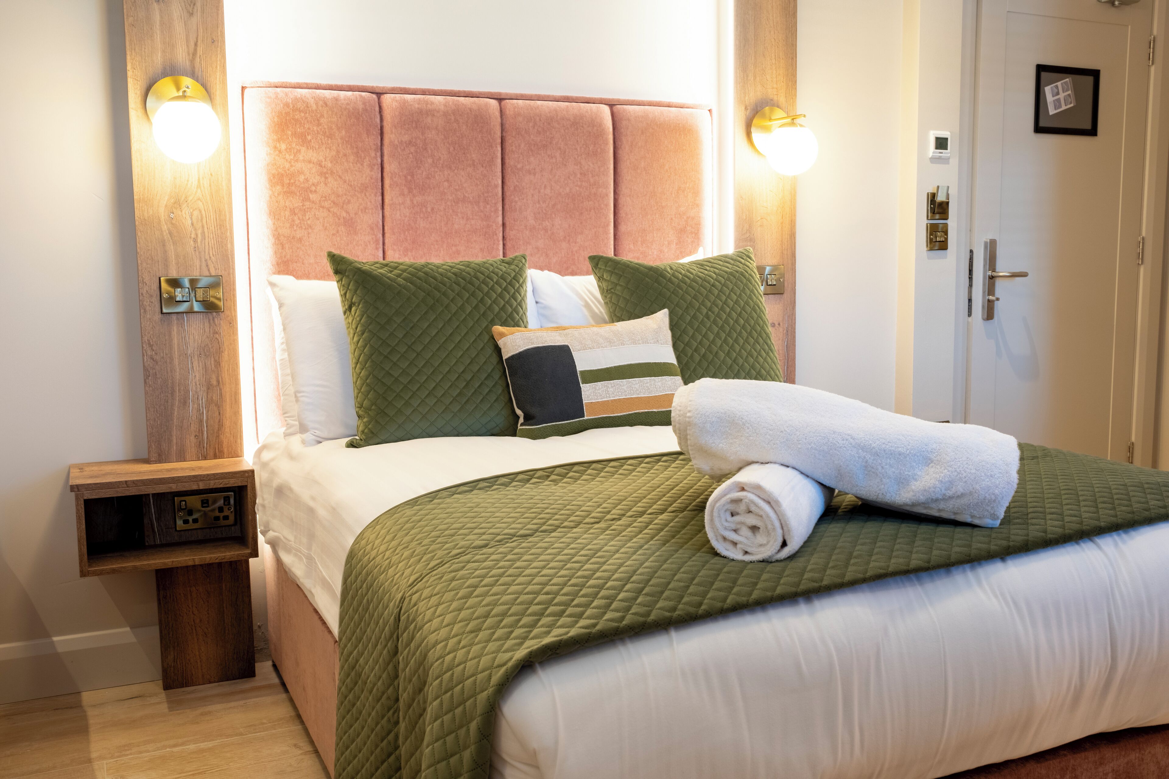 A neatly made bed with green bedding, a white pillow, and a rolled white towel.