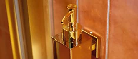 Objeto rectangular dorado, de metal, fijado a la pared, posiblemente un adorno de baño o un elemento funcional.