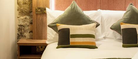 A neatly made bed with green bedding, a wooden nightstand, and a stone wall with a wooden panel above it.