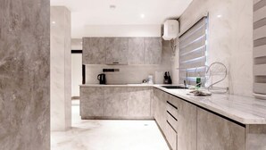 A modern kitchen with marble countertops, built-in cabinets, and a central island. - The Vattern Apartments (Abuja)