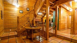 A wooden interior with a staircase, a round wooden table, and a green door. - Talako Lodge|4+BD|4BTH|16 Guest|Hot Tub|3 Story|Pool table (Broken Bow)