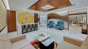 A modern hotel lobby with a reception desk, seating area, and a view into the dining area.