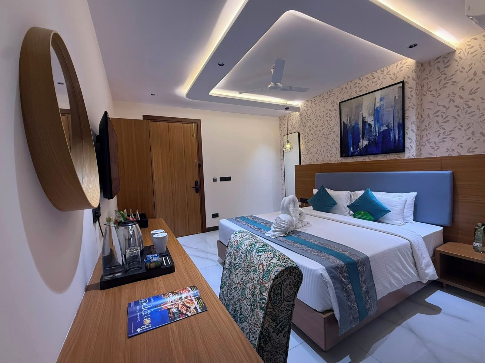 A hotel room with a bed, bedside table, desk, and a large mirror.