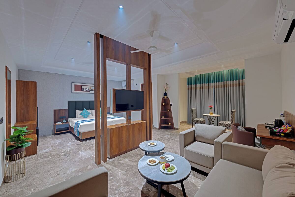 Ein modernes Hotelzimmer mit Bett, Fernseher, Esstisch mit Tellern und einer Sitzecke mit Sofa und Sesseln.