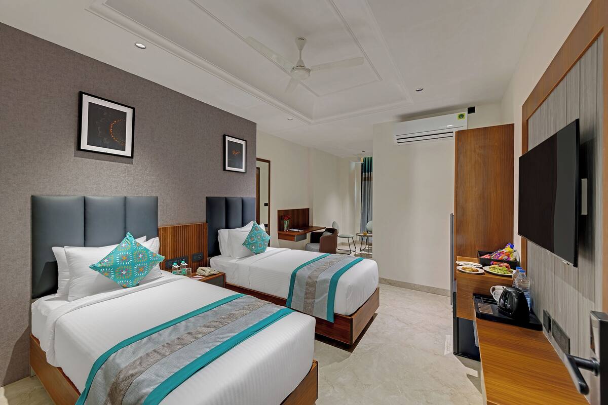 Ein Hotelzimmer mit zwei Betten, einem Fernseher, einem Schreibtisch mit Stuhl und einem durchgegangenen Tür angedeuteten Badezimmer.