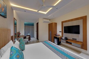Habitación de hotel con cama, televisor, escritorio y una computadora, además de una silla.