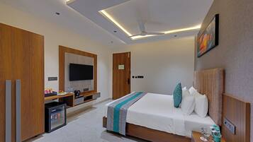 A modern hotel room with a bed, a television, a minibar, and a ceiling fan.