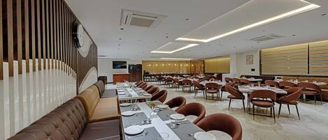 A spacious dining area with long tables, cushioned seating, and modern lighting fixtures.