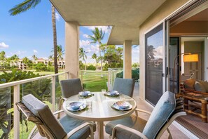 A balcony with a round table set for four, surrounded by cushioned chairs, overlooking a golf course and palm trees. - Vista Waikoloa G203: Luxury Condo in Waikoloa Resort: AC, Elevators, Views! (Waikoloa)