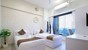 Habitación de hotel con dos camas, un escritorio, una planta en maceta y un ventanal con persianas.