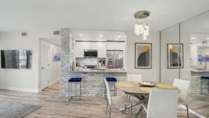 A modern kitchen with white cabinets, a central island, and a dining area with a round table and chairs. - 🏖️Beachfront Community🌴Land's End 1-206☀Heated Pool/Hot Tub🐬Bay Views (Treasure Island)