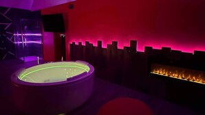Une salle de spa moderne dotée d’un bain à remous chauffé, d’un téléviseur fixé au mur et d’un foyer.