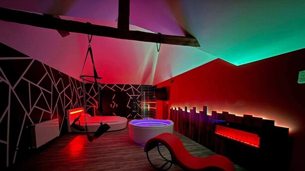 Une pièce moderne avec des motifs géométriques sur les murs, un fauteuil suspendu, un espace salon circulaire et un plafond en bois.