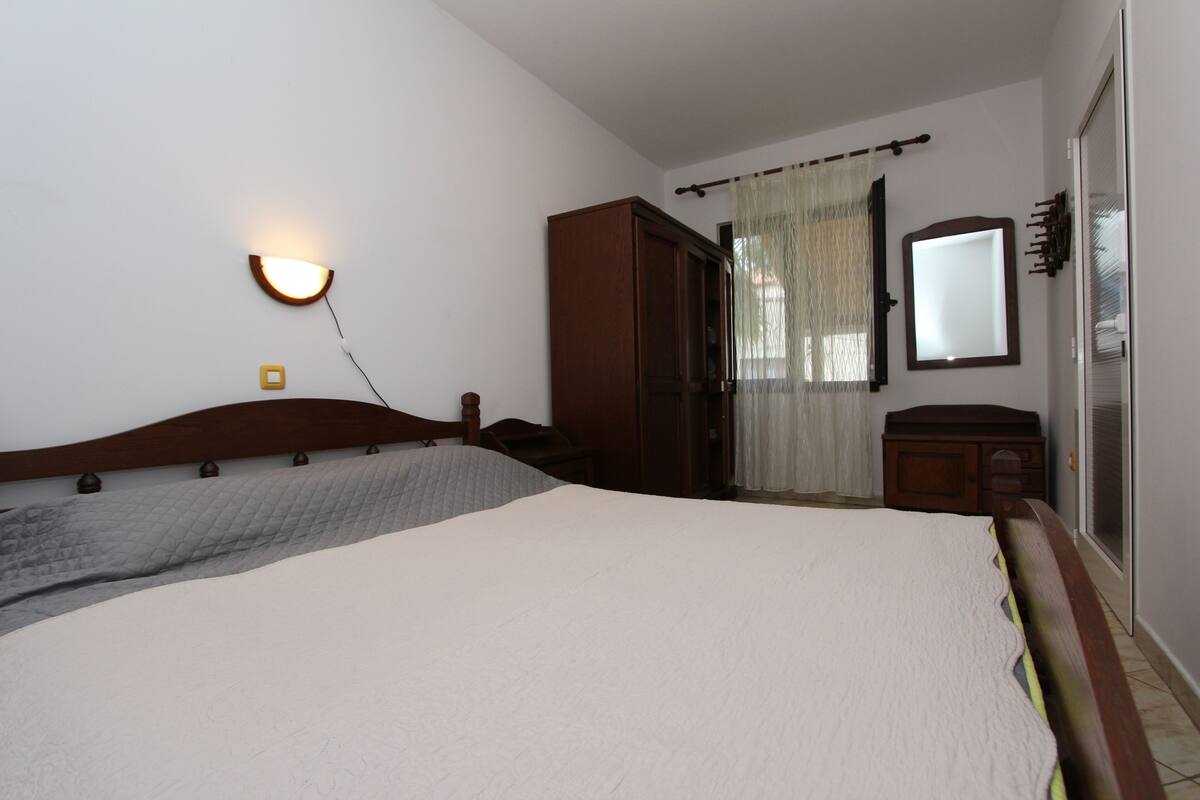 A bedroom with a large bed, a bedside table, a wardrobe, a mirror, and a wall-mounted light fixture.