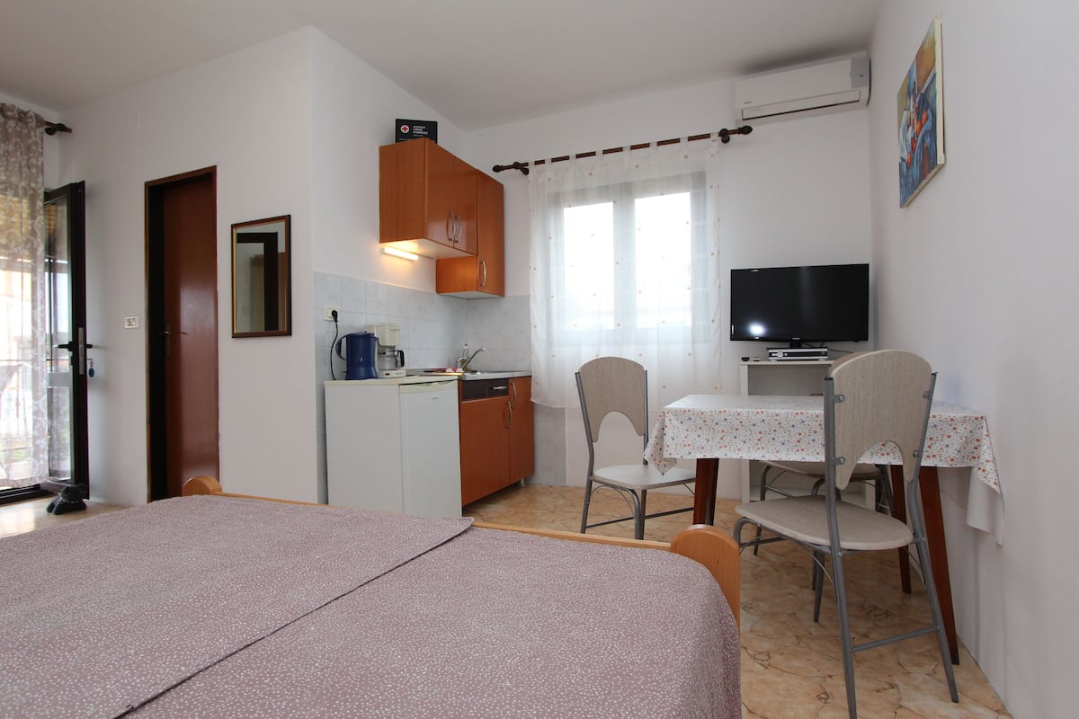 A compact room with a bed, kitchenette, dining area, and a TV.
