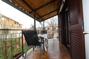 A covered balcony with a table and chairs, a view of buildings, and a door with a metal shutter. - Apartments Rosanna 2 (Rovinj)