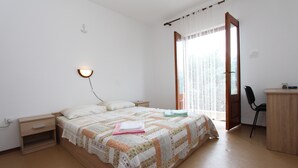 Camera da letto con letto, comodino, lampada, sedia, scrivania e finestra con tende.