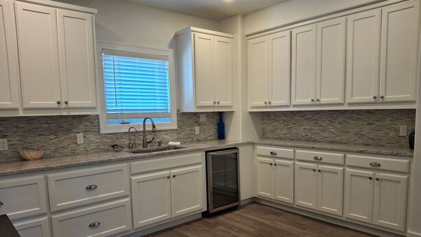 A kitchen with white cabinets, a built-in dishwasher, and a window with blinds.