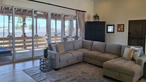 Ein geräumiges Wohnzimmer mit einer großen Eckcouch, einem Deckenventilator und Blick ins Freie durch große Schiebeglastüren.