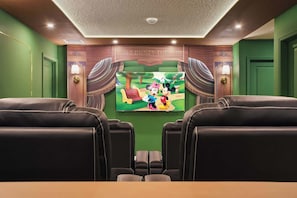 Uma sala de cinema com paredes verdes, uma tela grande e assentos de couro preto.