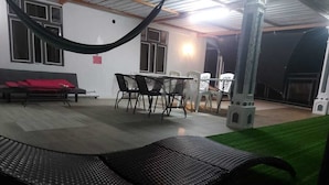 An outdoor patio with a black lounge chair, a dining table with chairs, a sofa with red cushions, and a small white playhouse. - ENTRE VALLEE (Rodrigues Island)