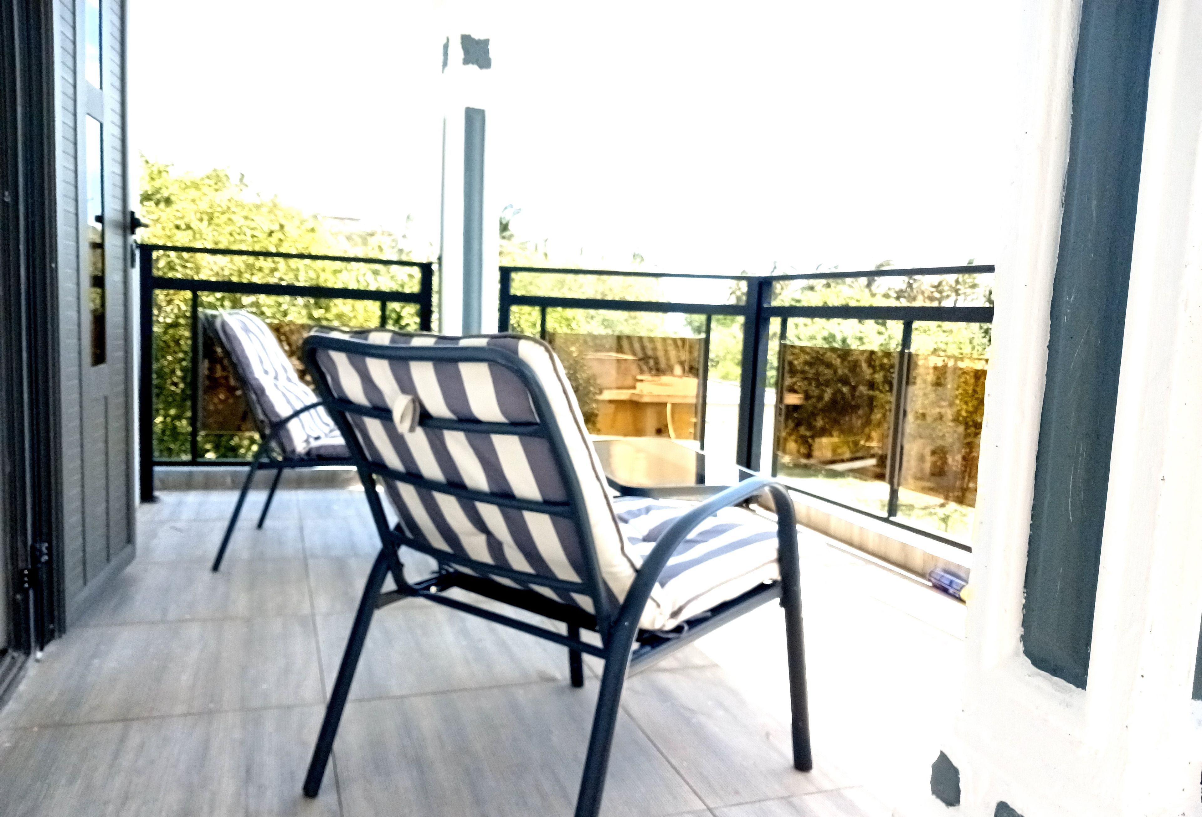 Een balkon met twee streepstoelen en een tafel.