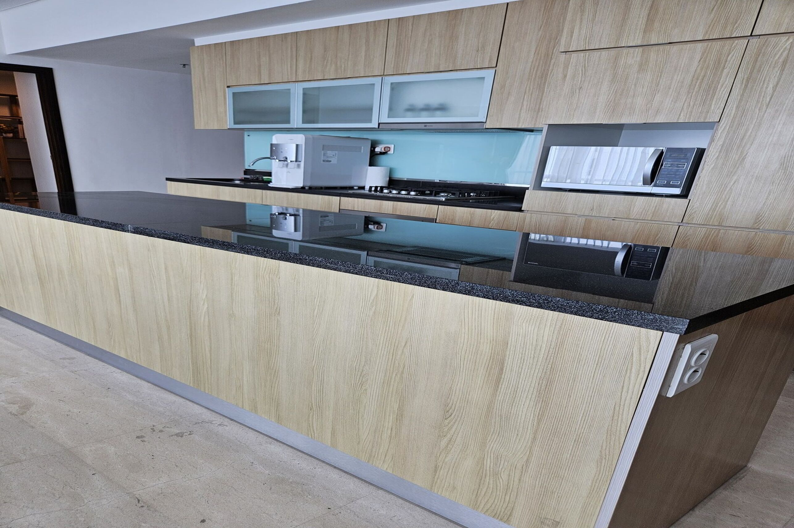 A modern kitchen with wooden cabinets, a black countertop, and built-in appliances including a coffee maker and microwave.