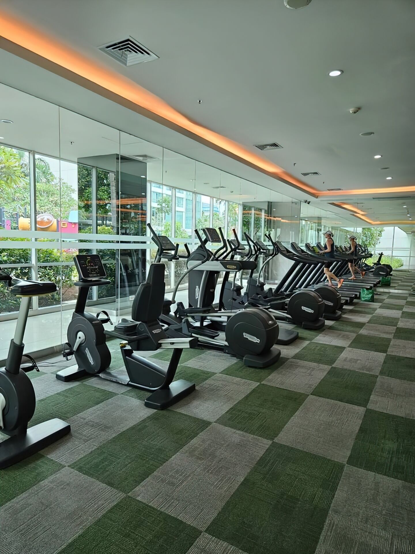 A gym with multiple treadmills and stationary bikes, large windows, and a checkered floor.