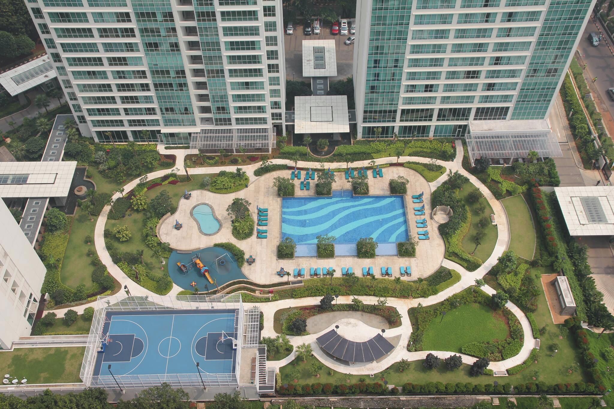 A high-rise building with a rooftop pool, a basketball court, and landscaped gardens.