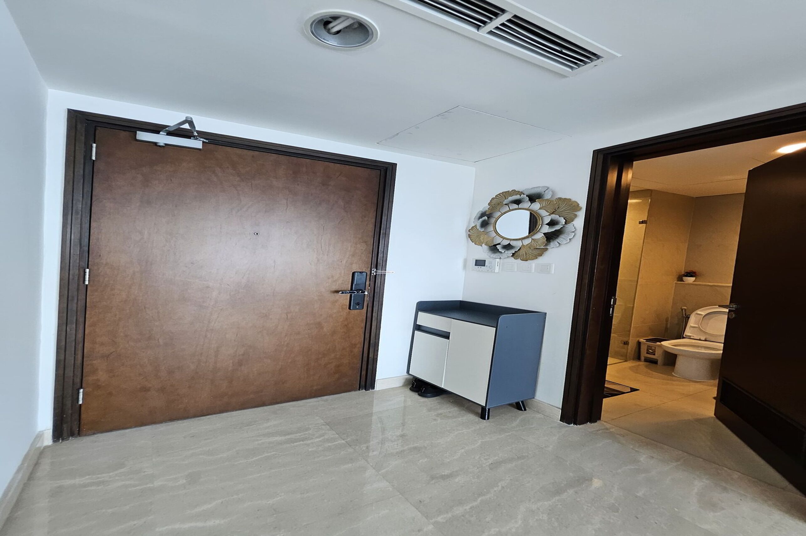 A hallway with a wooden door, a desk, and a bathroom visible through an open door.