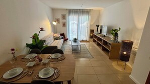 Een moderne woonkamer met een eethoek, een bank, een televisie en een plant.