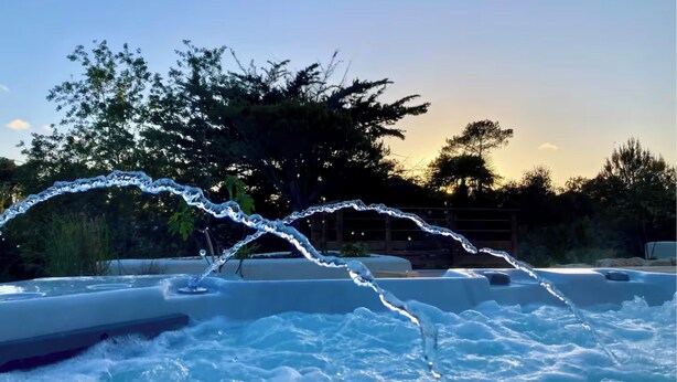 Ein Whirlpool mit in Bewegung befindlichen Wasserstrahlen, umgeben von Bäumen und blauem Himmel.