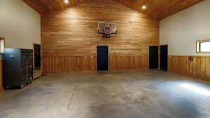 Et rummeligt indendørs område med træloft, basketballkurv og et opbevaringsskab til venstre.