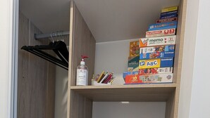 Un placard avec des étagères contenant divers objets, notamment une bouteille de désinfectant, un ensemble de cintres et plusieurs boîtes de jouets pour enfants.