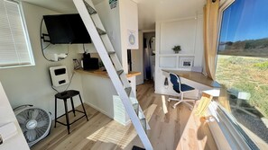 A compact room with a desk, chair, and a large window offering a view of the outdoors.