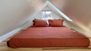 Une chambre avec un plafond en pente, une fenêtre et un lit recouvert d’une couette rouge.